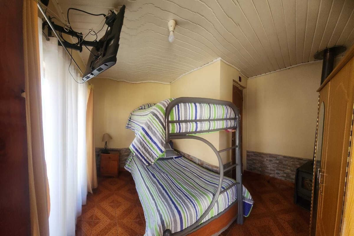 A bunk bed with striped bedding in a room with patterned flooring and a wooden wardrobe.