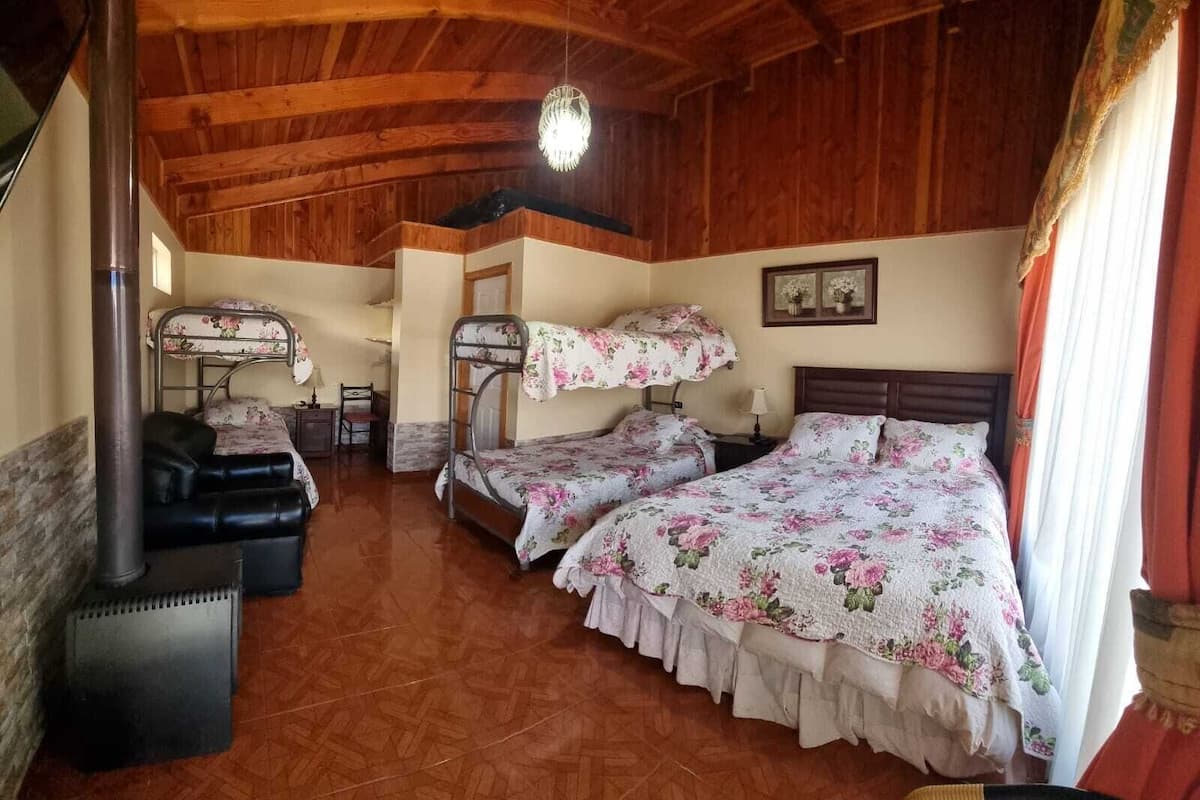 A rustic room with wooden ceilings, two bunk beds with floral bedding, a desk, and a chair.
