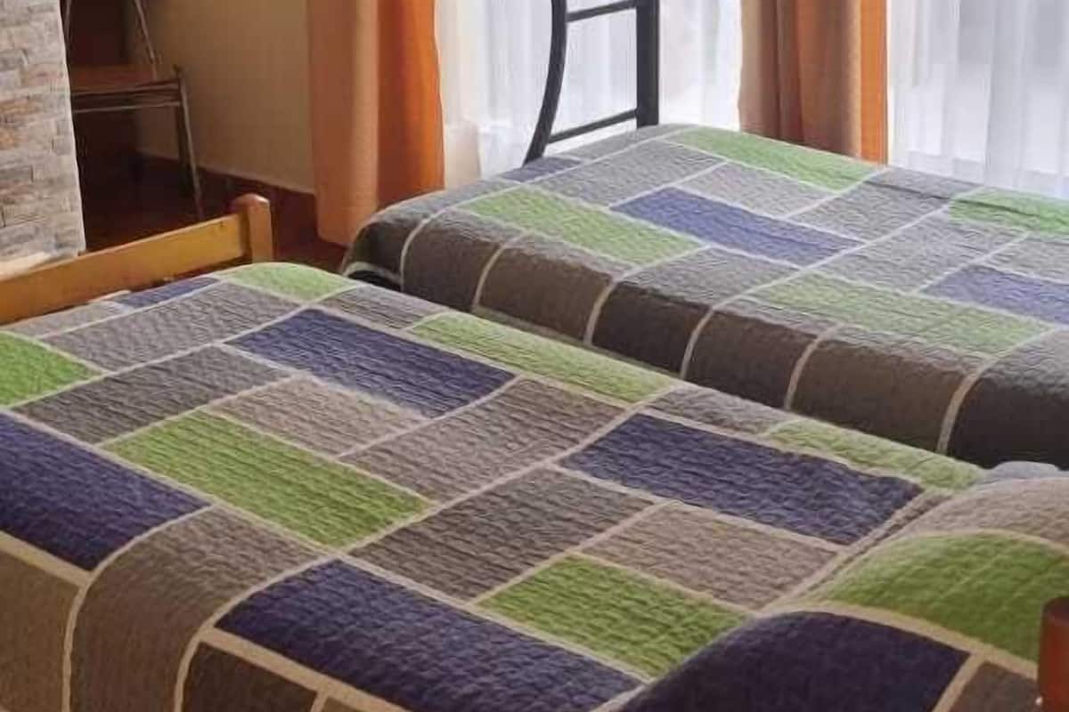 A bunk bed with a colorful quilt, a chair, and a window with curtains.