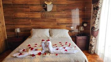 A bed with rose petals and a towel sculpture, wooden panel walls, and a nightstand with a lamp.