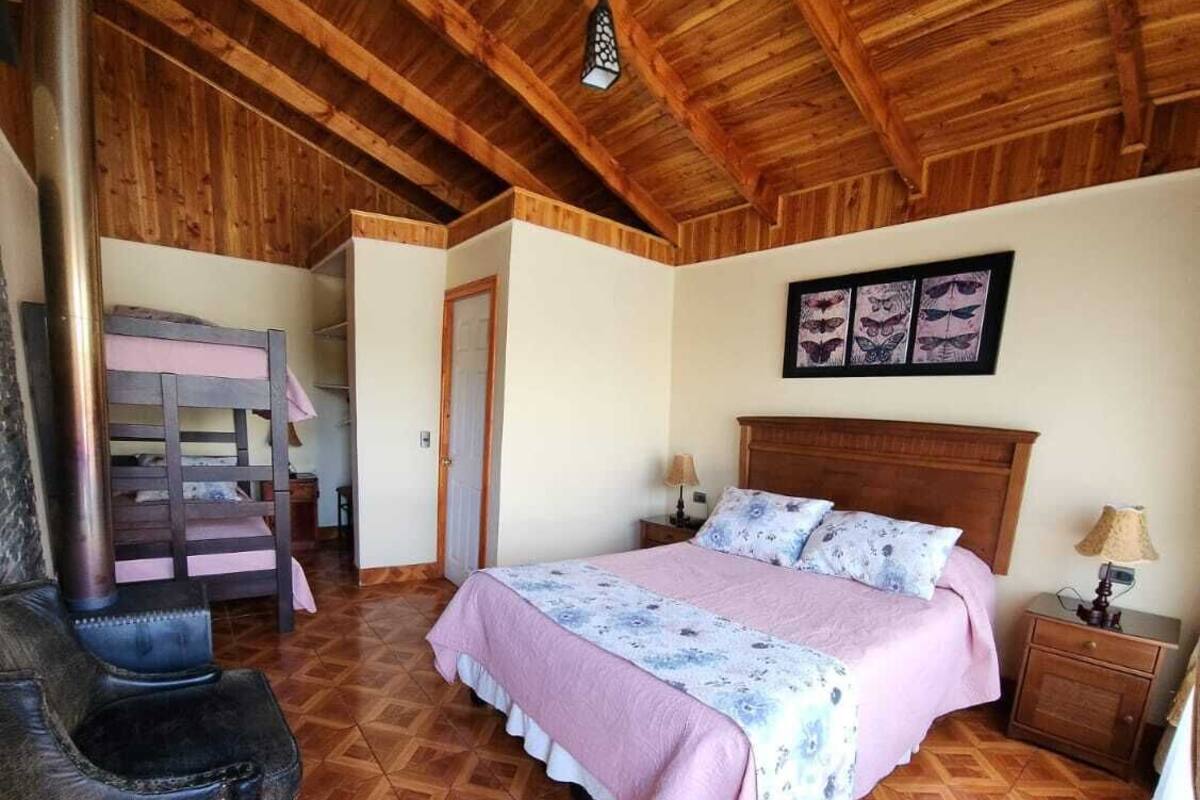 A bedroom with a wooden ceiling, a bed with floral bedding, a nightstand, and a chair.
