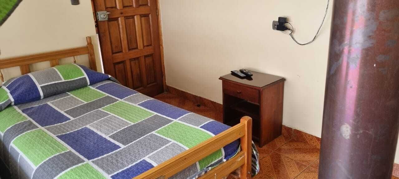A bedroom with a wooden bed, a nightstand, a door, and a wall socket.