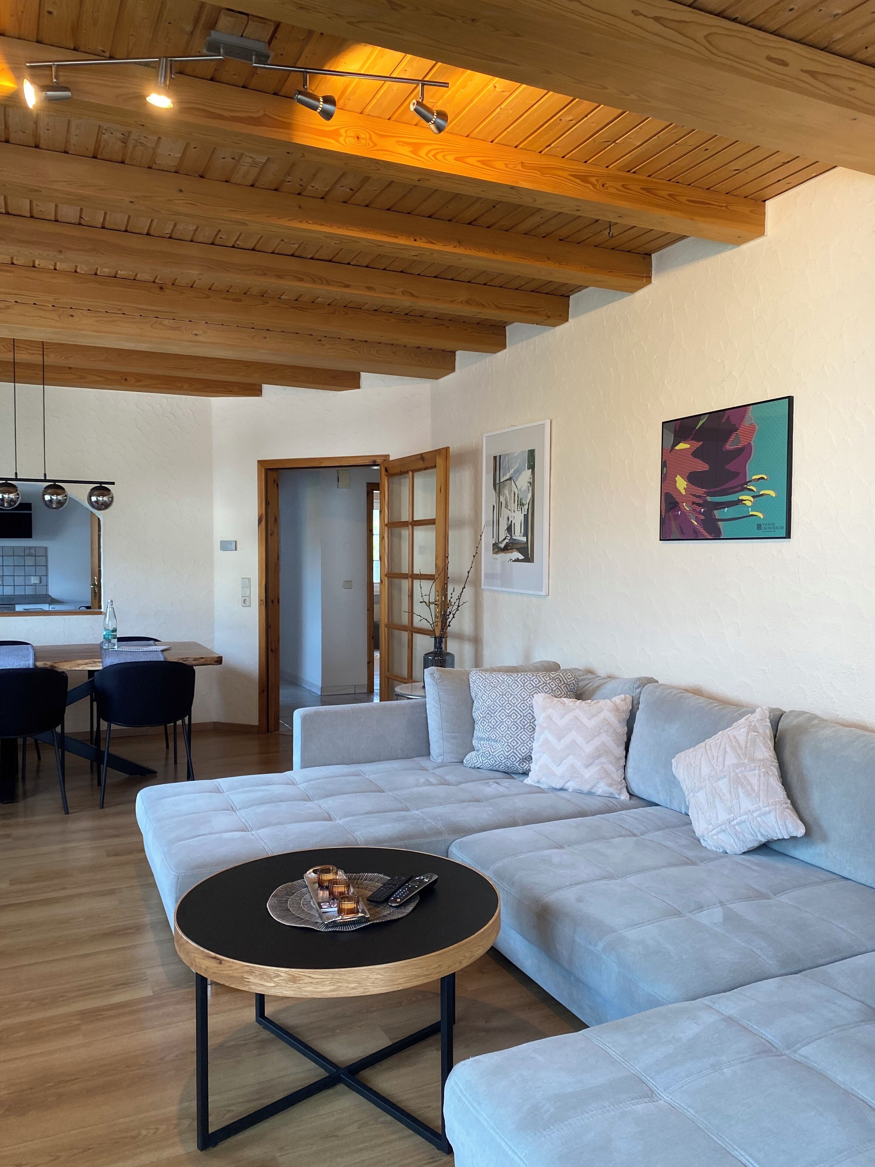 Un salon moderne avec un canapé gris clair, une table basse ronde et un plafond en bois.