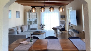A dining area with a wooden table and benches, a sofa, and a TV in the background. - Apartment Sonnenlay OG (Brauneberg)
