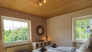 A bedroom with a large bed, two windows, a wooden ceiling, and a radiator. - Apartment Sonnenlay OG (Brauneberg)