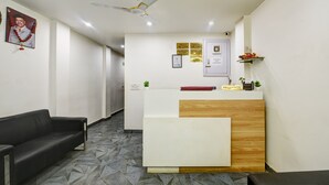 A reception area with a reception desk, a black leather sofa, a ceiling fan, and a patterned floor. - The Sunrise Vista (New Delhi)