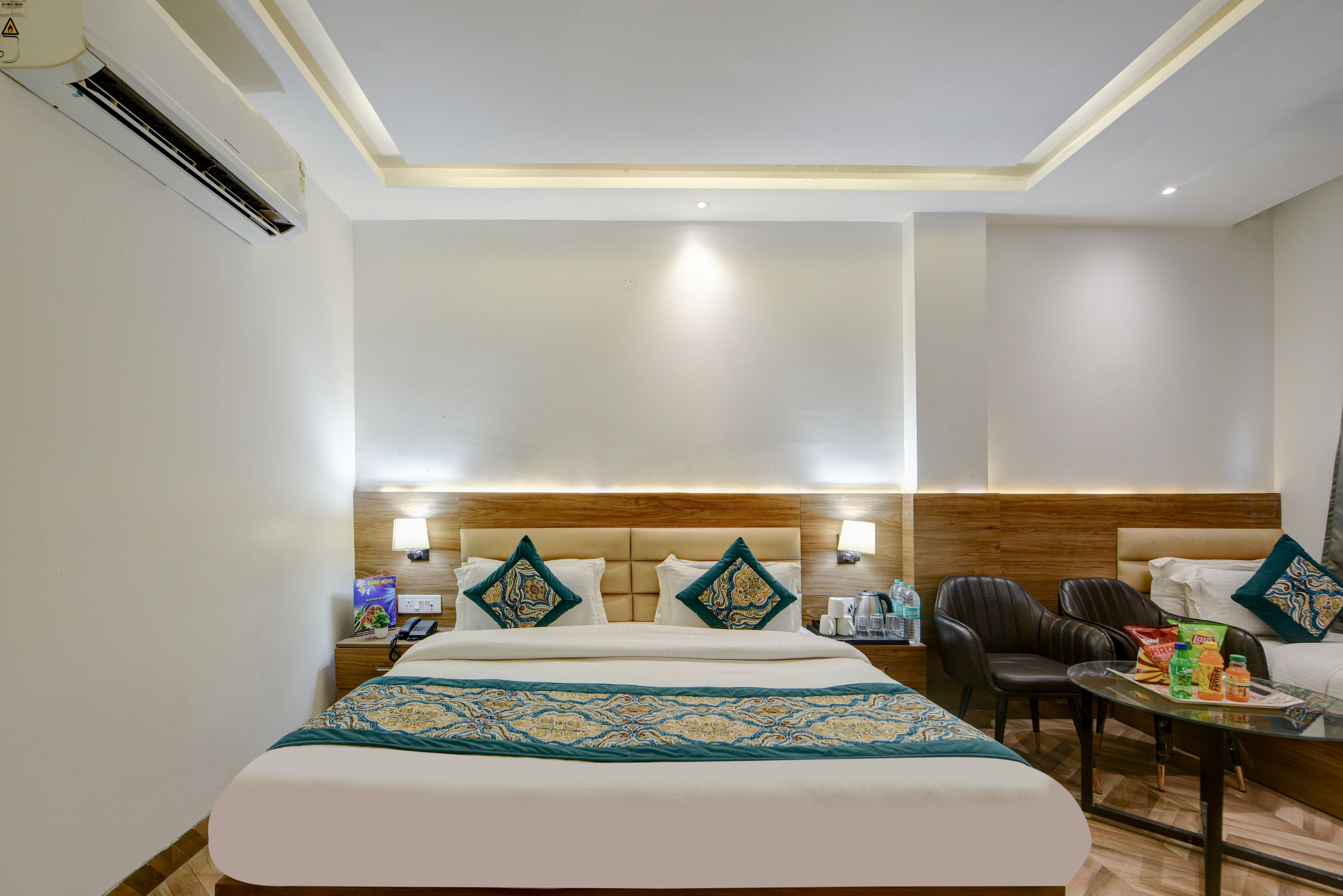 Habitación de hotel con una cama grande, cabecera de madera, una mesita con sillas y un minibar.