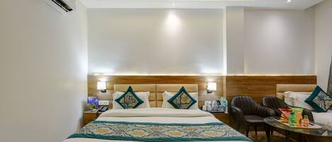 Habitación de hotel con una cama grande, cabecera de madera, una mesita con sillas y un minibar.