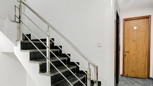 A staircase with metal railings leading to a landing, a wooden door, and patterned flooring. - The Sunrise Vista (New Delhi)