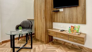 A modern room with a herringbone wooden floor, a glass table with a chair, a wooden cabinet, and a mounted TV. - The Sunrise Vista (New Delhi)