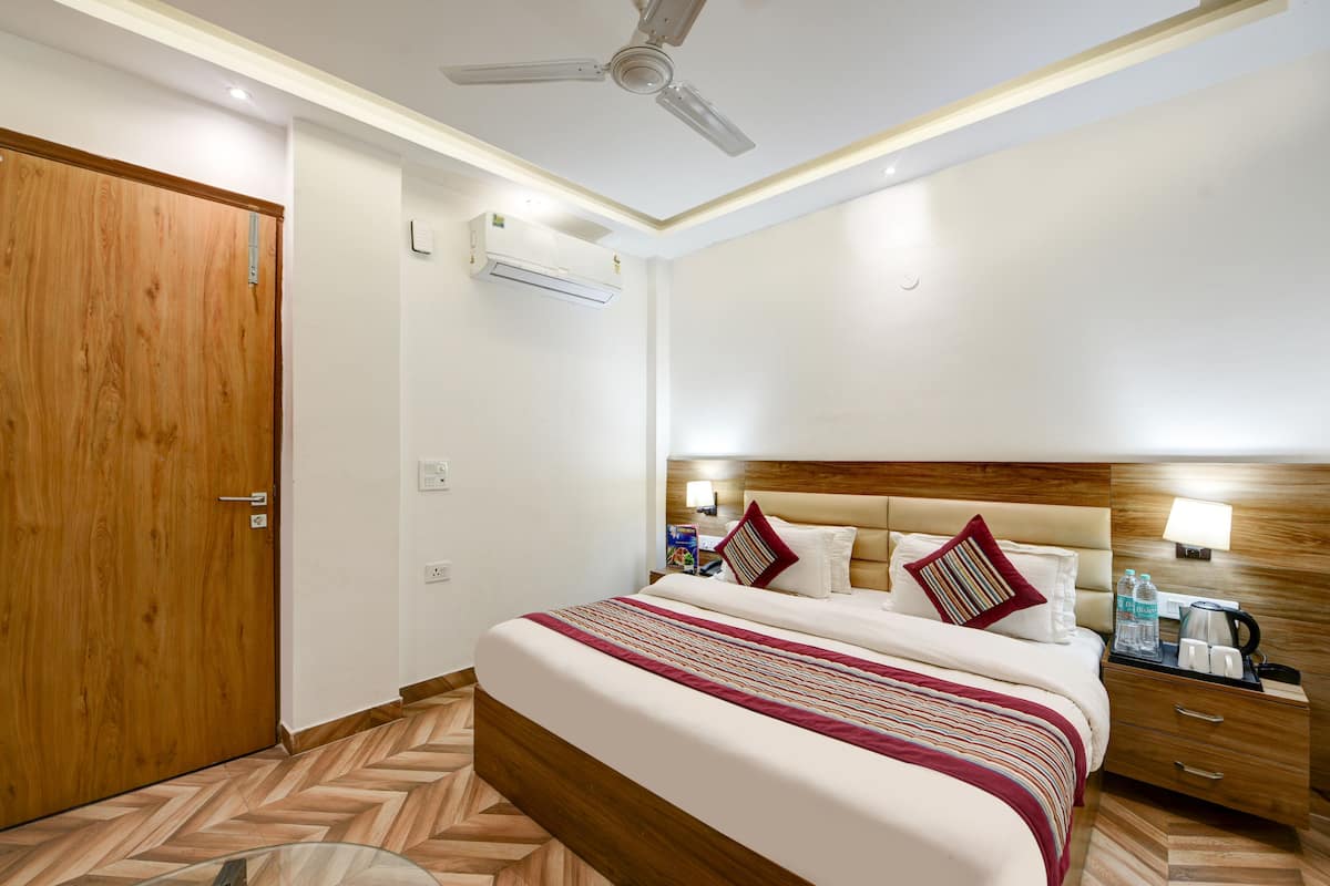 Une chambre d’hôtel avec une porte en bois, un lit recouvert d’une courtepointe à rayures, une table de chevet avec une lampe et un ventilateur de plafond.