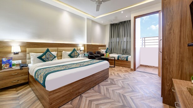A hotel room with a large bed, a ceiling fan, a wooden headboard, a nightstand, a desk, and a view of the outdoors. - The Sunrise Vista (New Delhi)