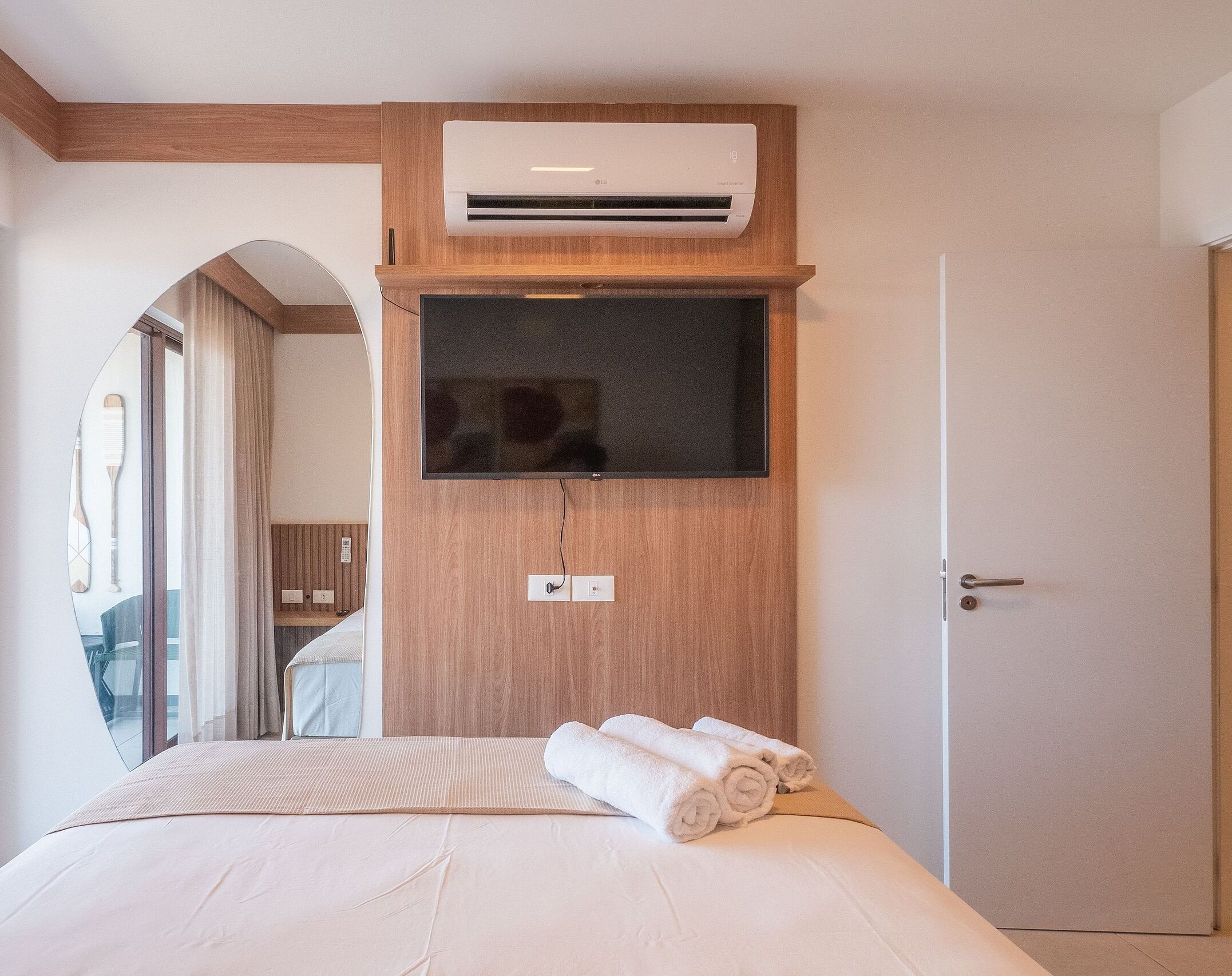 Een hotelkamer met een bed, een wandtelevisie, een airconditioningsysteem en een deur.