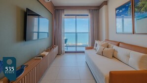 Ein Hotelzimmer mit großem Fenster, einem Flachbildfernseher, einer Couch und einem Holztischchen.