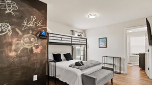 A bunk bed room with a white bed, a gray bench, and a chalkboard wall with drawings. - Modern 4BR Athens Retreat | Massage Chairs | Sleeps 9 | Near UGA & Downtown (Athens)