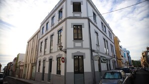 Un edificio en esquina con varias ventanas y una puerta, situado en una calle con automóviles estacionados.