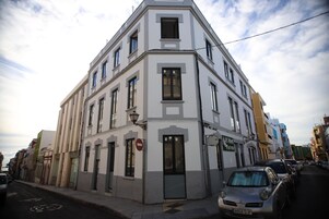 Un edificio en esquina con varias ventanas y una puerta, situado en una calle con automóviles estacionados.