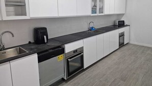 Una cocina moderna con armarios blancos, encimera negra, lavavajillas, horno, fregadero y microondas.