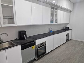 Una cocina moderna con armarios blancos, encimera negra, lavavajillas, horno, fregadero y microondas.