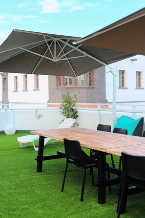An outdoor seating area with a wooden table, black chairs, a large umbrella, and a potted plant. - Las Palmas Nest Hostel (Las Palmas de Gran Canaria)