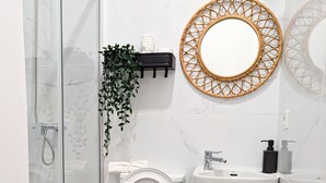 Un baño moderno con cabina de ducha de vidrio, inodoro, lavabo con espejo y un pequeño cubo de basura.