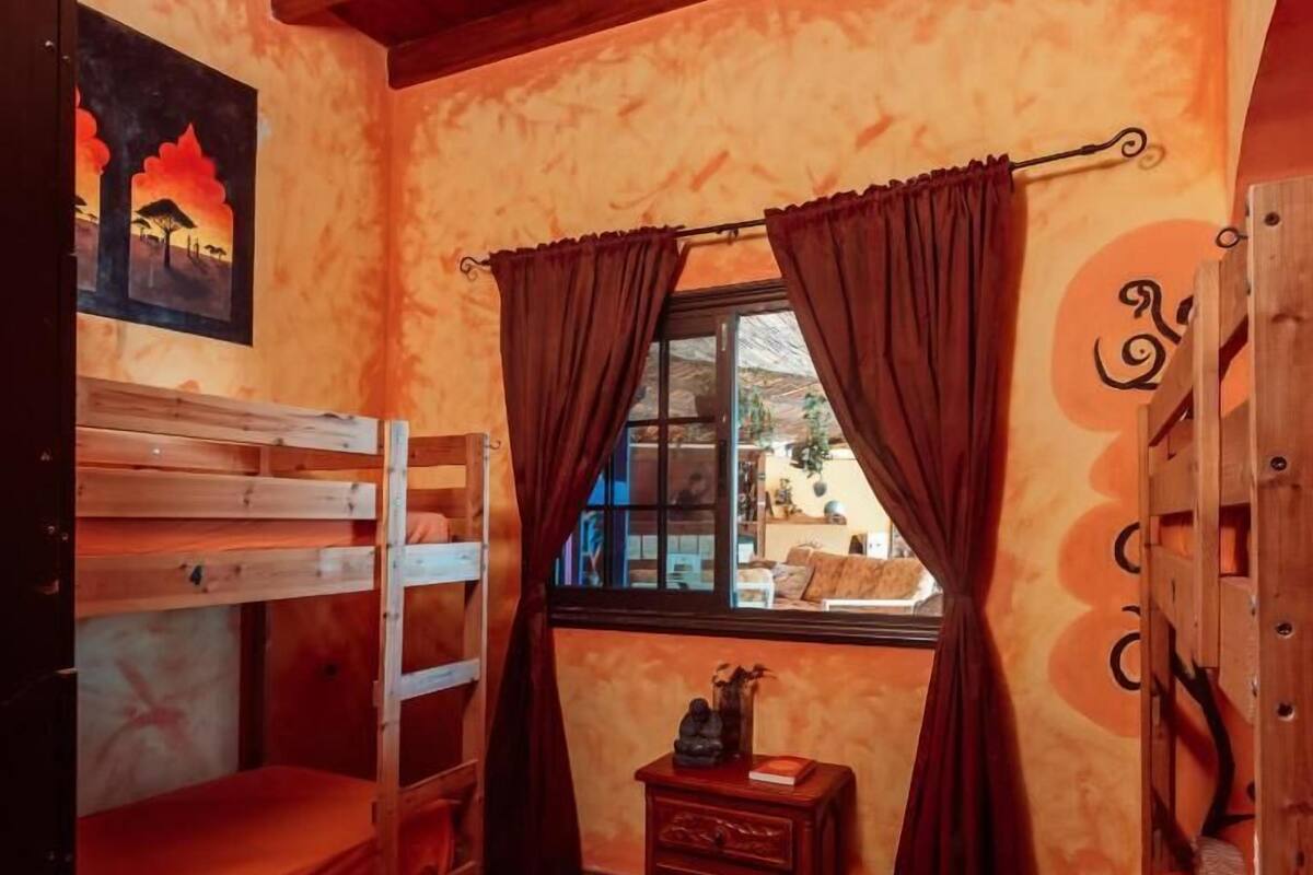 Una habitación acogedora con literas de madera, un pequeño cofre de madera y una ventana con cortinas.