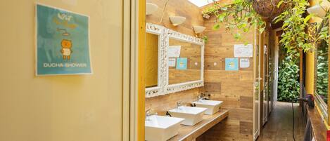 A wooden bathroom with three sinks, a large mirror, and a DUCHA shower sign.