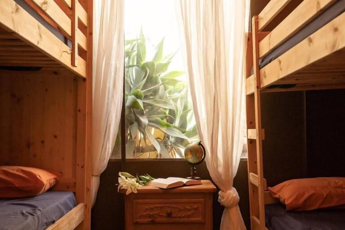 Una habitación pequeña y acogedora con dos literas, un aparador de madera, un globo terráqueo y una planta junto a la ventana.