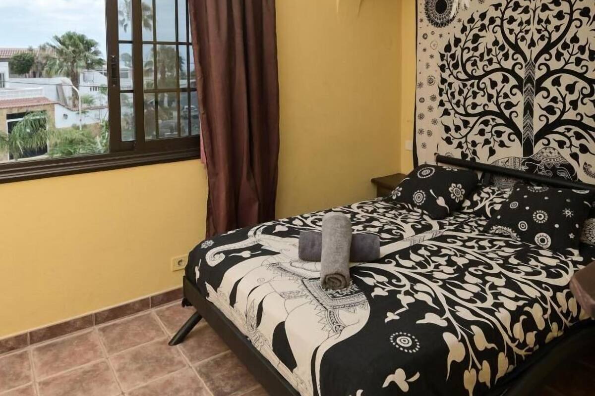 Un dormitorio con cama, ventana con cortinas, un tapiz decorativo y vistas al exterior.