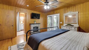 A bedroom with wooden walls, a ceiling fan, a fireplace, a bed, a dresser, and a TV. - Bear Brow Cabin. Amazing view from brow to valley below. (Mentone)