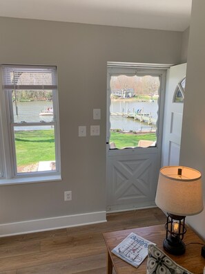 A room with a view of a lake, a door, and a lamp on a table.