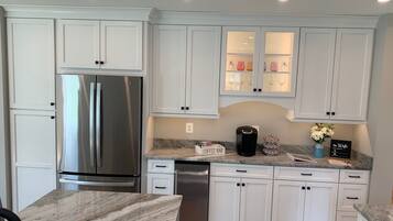 A modern kitchen with white cabinetry, stainless steel appliances, and a marble countertop.