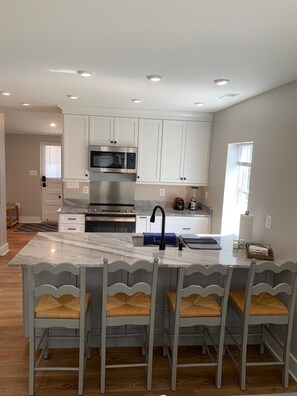 A modern kitchen with white cabinets, a stainless steel oven, a microwave, and a large island with bar stools.