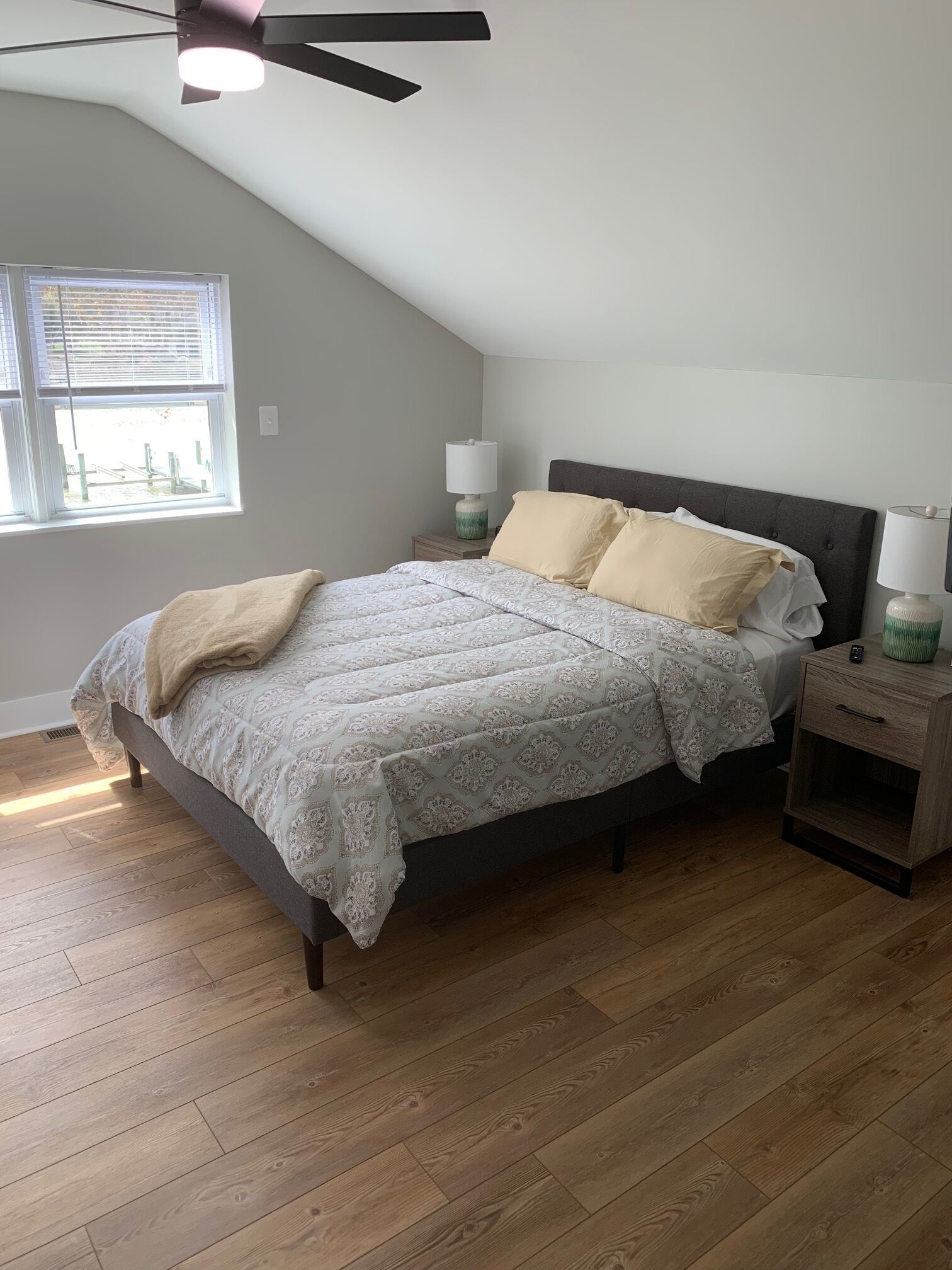 A bedroom with a bed, bedside tables, a ceiling fan, and a window with blinds.