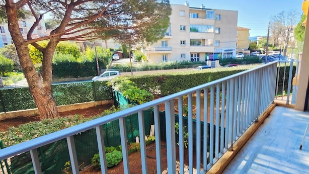 A balcony with a view of a residential street, a tree, and a building in the background.