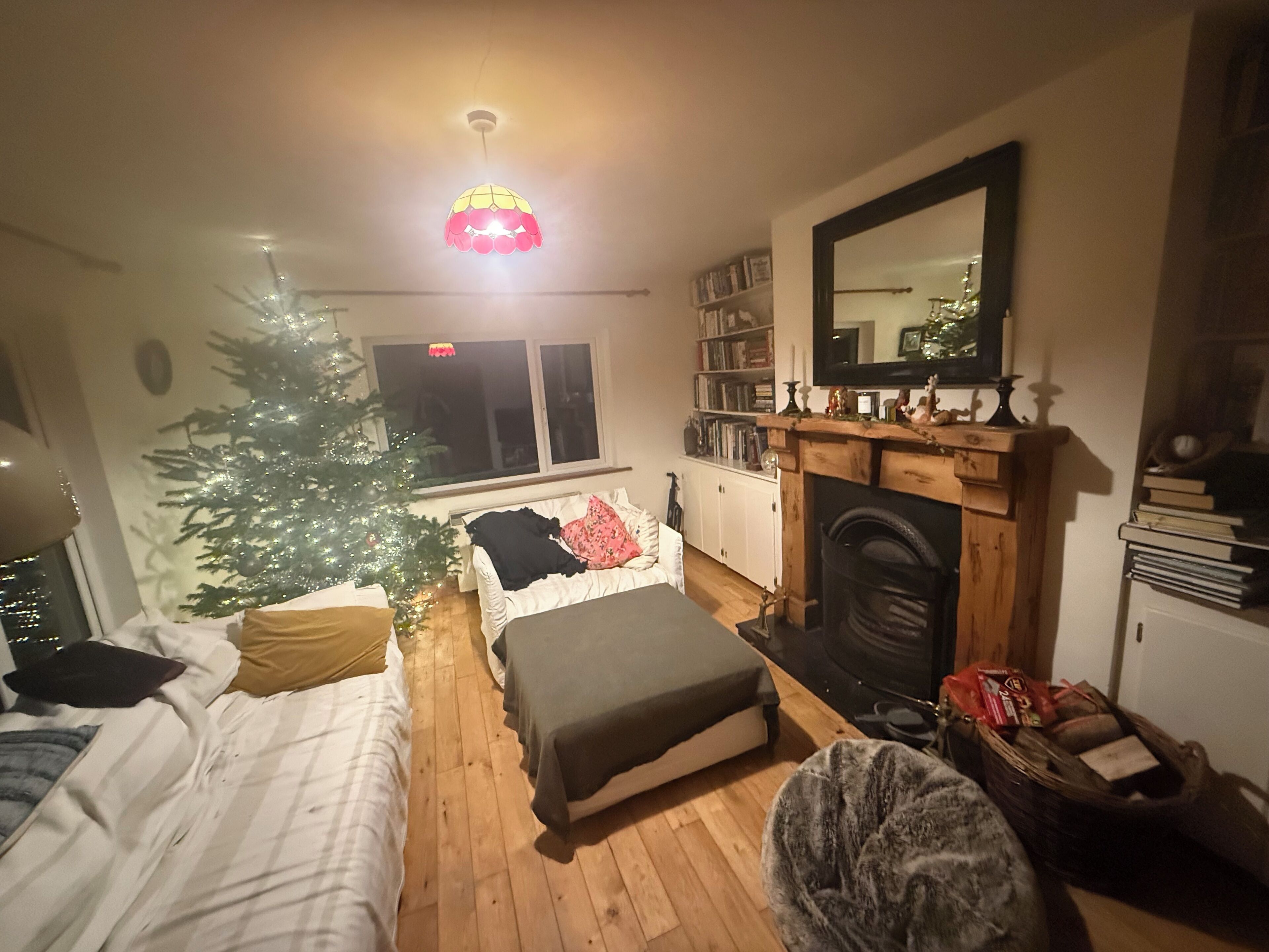 A cozy living room with a fireplace, a Christmas tree, and a bookshelf.