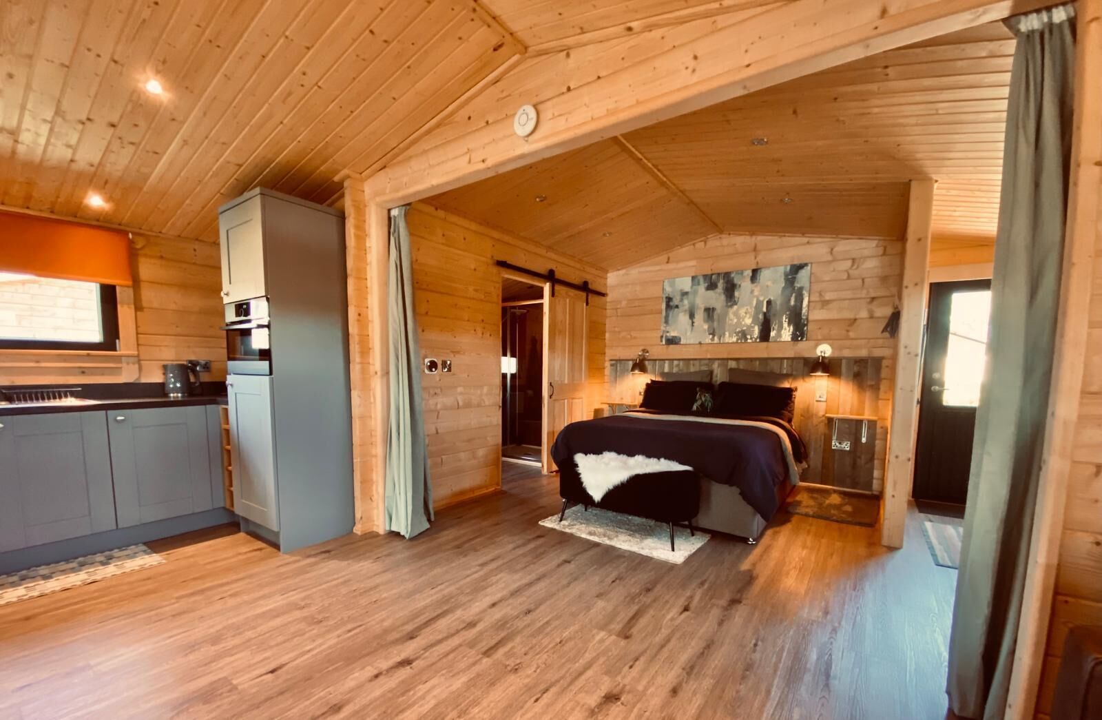 A log cabin interior with a kitchen, a bed, and a bathroom.