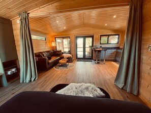 A cozy cabin interior with a wooden ceiling, a sofa, a dining table, and a kitchen area.