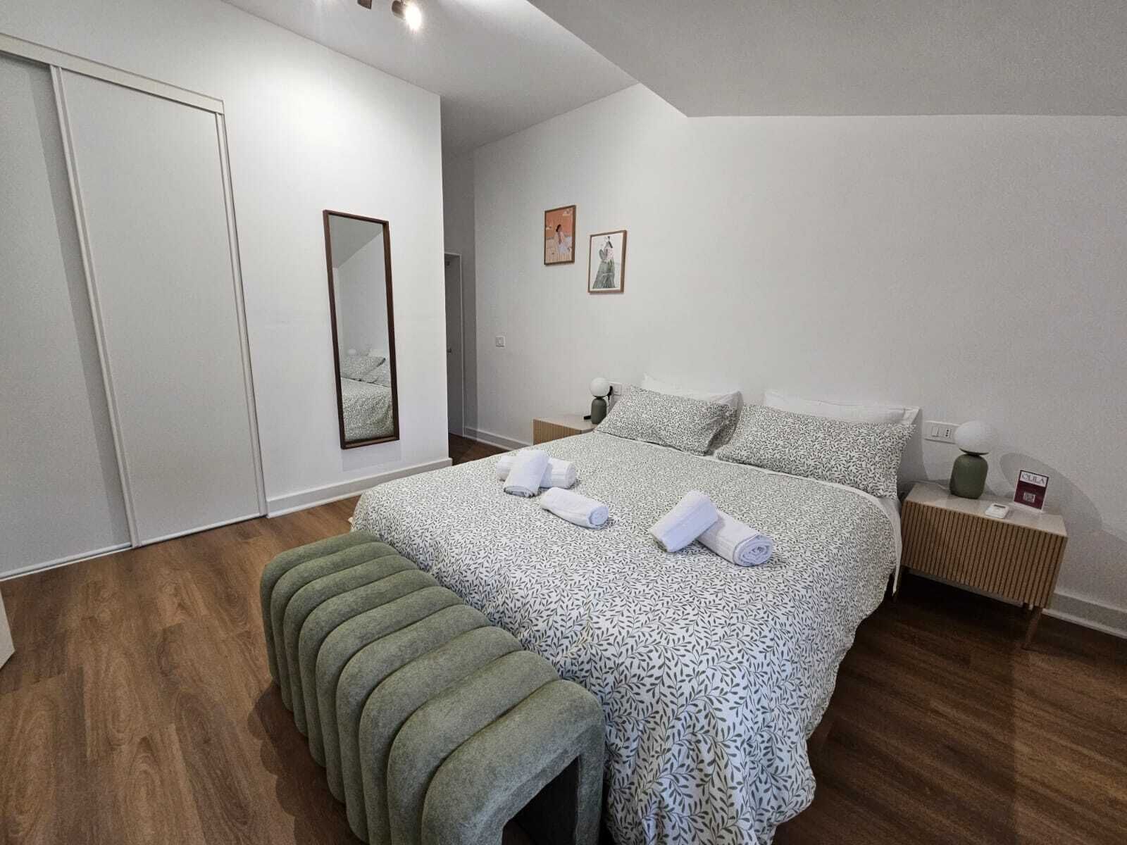 A bedroom with a bed, a bench, a nightstand, and a mirror.