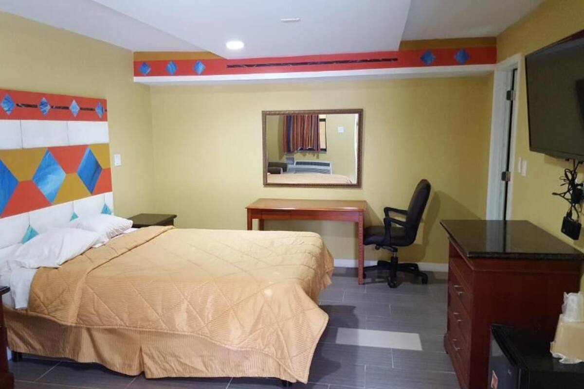 A hotel room with a bed, a desk, a chair, a TV, and a dresser.