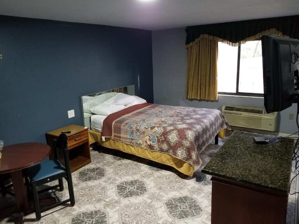 A bedroom with a bed, a desk, a chair, and a television.