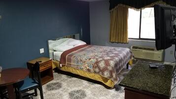 A bedroom with a bed, a desk, a chair, and a television.