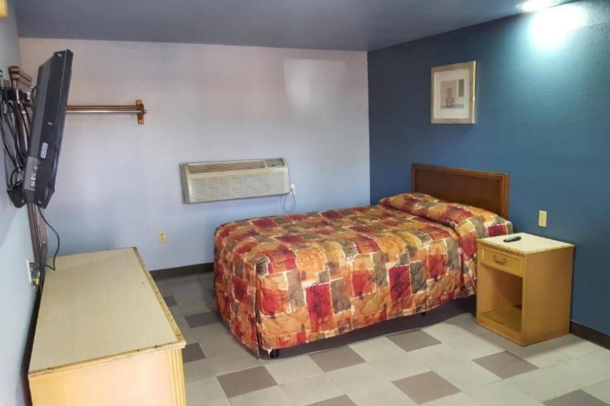 A bedroom with a bed, a bedside table, a TV, and an air conditioning unit.