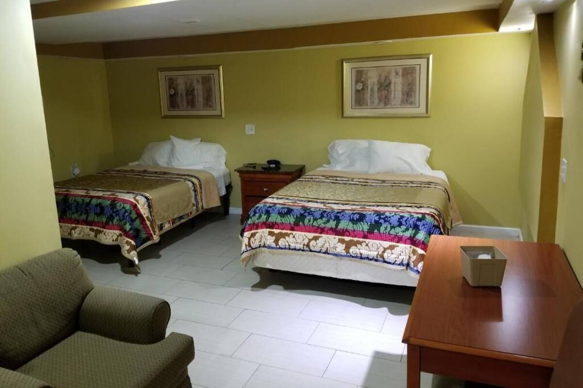 A hotel room with two beds, a sofa, a wooden table, and artwork on the walls.