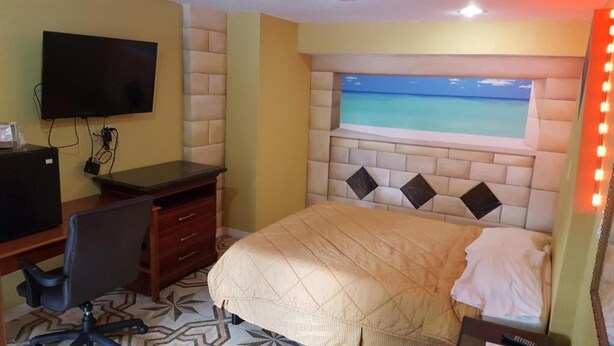 A bedroom with a bed, a desk with a chair, a TV, and a window with a view of the ocean. - Budget Motel (Orlando)