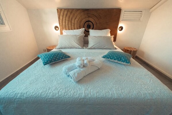 A neatly made bed with a patterned bedspread, two pillows with a blue and white design, and a pair of folded towels. - Villa d'Exception avec Piscine - 3 Min de la Plage 4 chambres climatisées (Sainte-Anne)