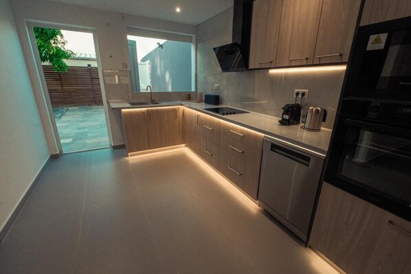 A modern kitchen with wooden cabinets, a built-in oven, and a dishwasher. - Villa d'Exception avec Piscine - 3 Min de la Plage 4 chambres climatisées (Sainte-Anne)
