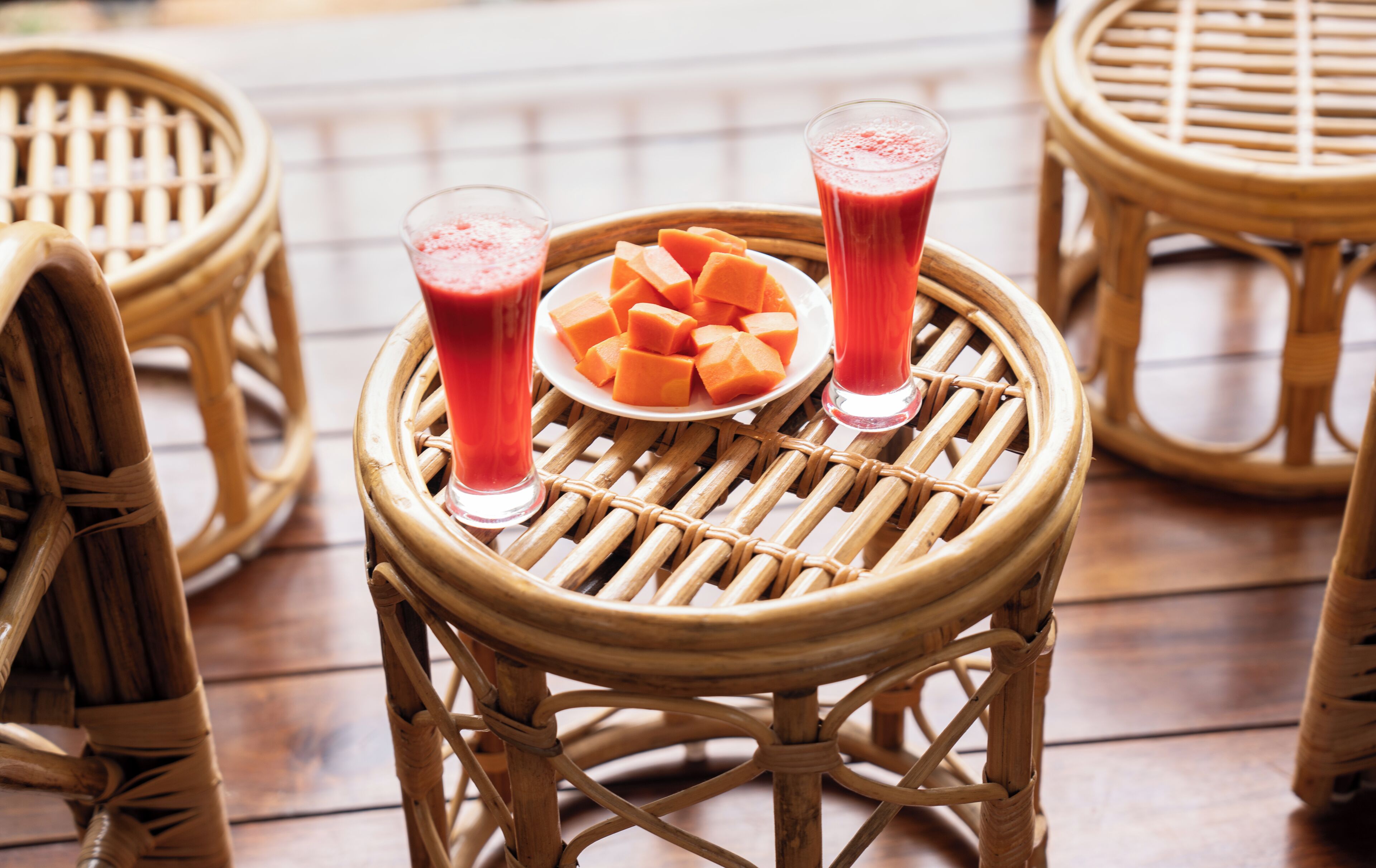A wicker table with two glasses of red beverage and a plate of orange cubes.