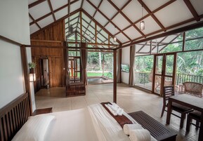 Una habitación amplia con una cama grande, vigas de madera en el techo y un balcón con muebles de mimbre.