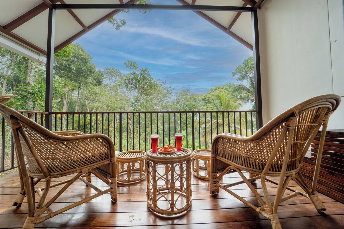 Un espacio de estar techado al aire libre con mobiliario de mimbre y una mesa, con vistas a un jardín exuberante.